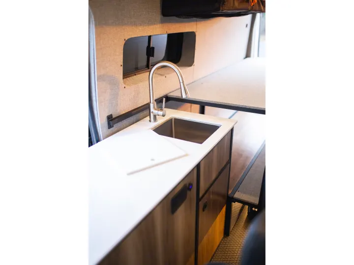 Step inside this rv rental: featuring a modern kitchen sink, white countertop, custom cabinets, and elevated bed.. Ford Transit 2021
