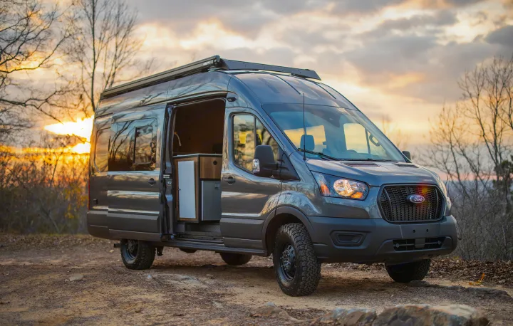 Grey Ford Transit rv rental camper van parked on a dirt path with an open door showing the modular interior.. Ford Transit 2021