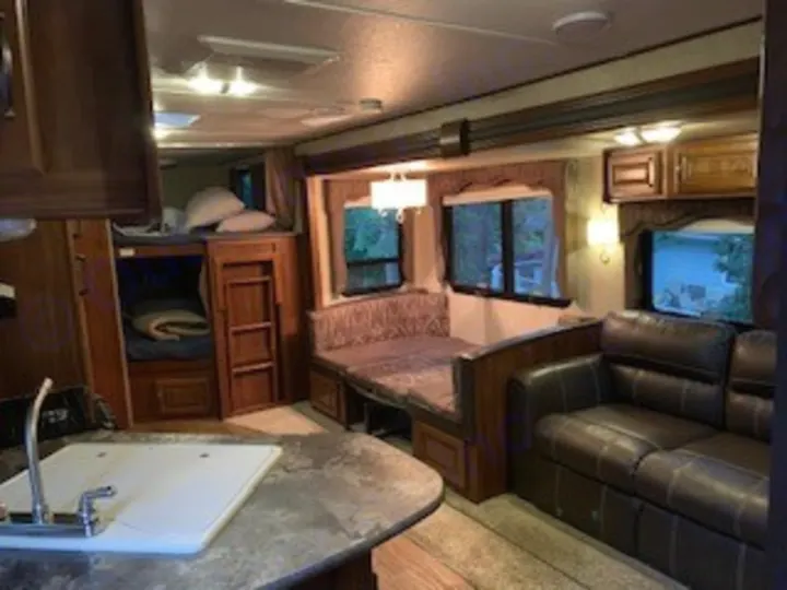 Inside this cozy RV rental: a kitchen counter, bunk beds, dinette, and sofa. Ideal for comfortable travel accommodations.. Keystone RV Cougar 2014