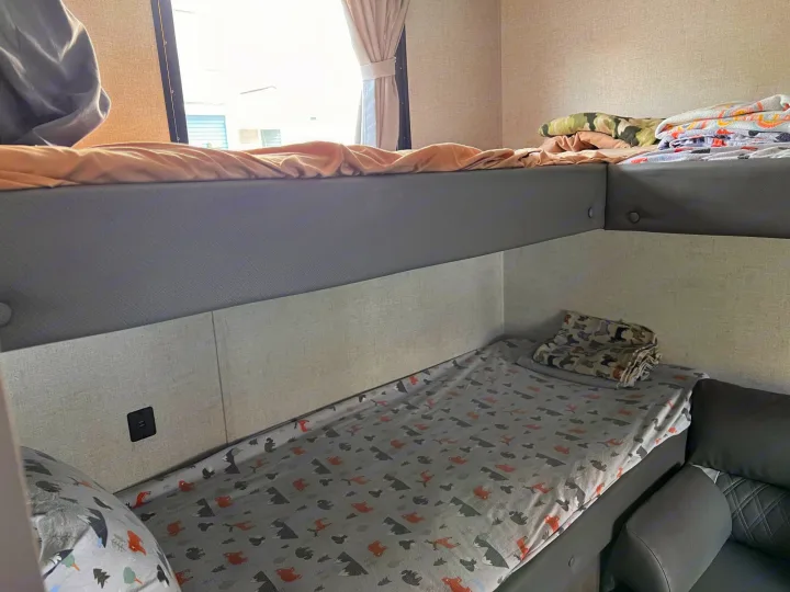 Inside an RV rental: cozy bunk beds with patterned and solid bedding, a window, and a wall outlet offer compact sleeping.. Forest River Wildwood X-Lite 2021
