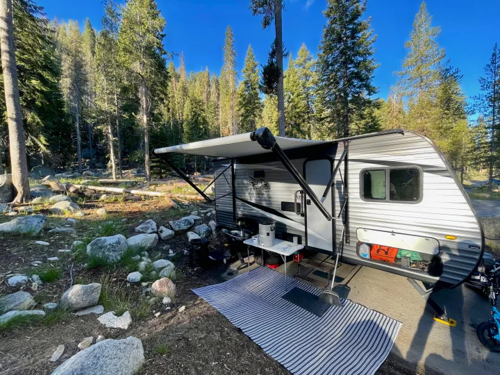 Spacious RV rental set up in a scenic forest campsite with an extended awning, ready for outdoor living.. Jayco Jay Flight 2021