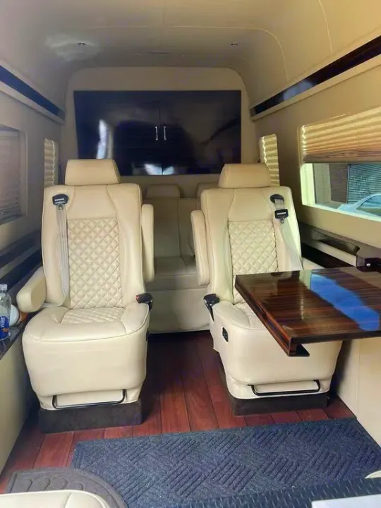 Step into luxury with this RV rental interior! Featuring plush cream captain's chairs, a rich wood floor, and custom table.. Mercedes-Benz Sprinter 2016