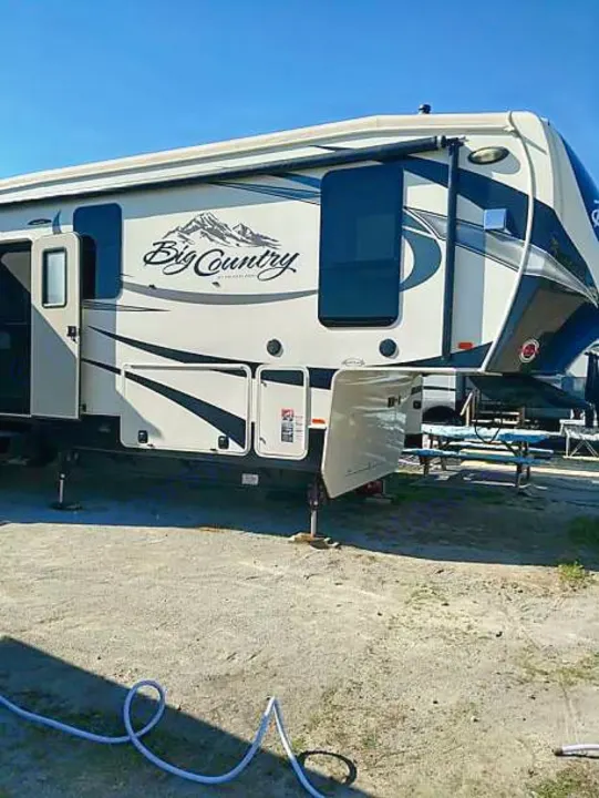 White "Big Country" fifth-wheel RV rental, parked on gravel under a blue sky, ready for outdoor camping.. Heartland Big Country 2016