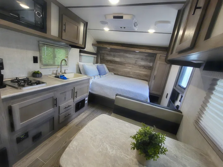 Modern RV rental interior: a clean kitchen with sink & stove, cozy bedroom, and wood-look floors for travel.. Gulf Stream Kingsport 2022