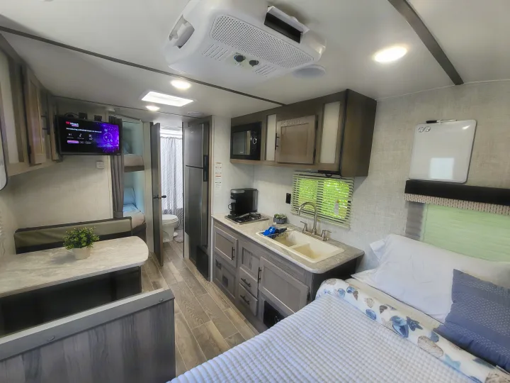 Spacious rv rental interior: bed, well-equipped kitchen (sink, microwave), dining table, TV, and compact bath.. Gulf Stream Kingsport 2022