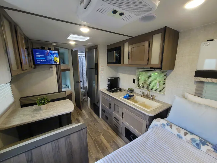 View inside a modern rv rental with a well-appointed kitchen, cozy dinette, main bed, and bunk beds visible.. Gulf Stream Kingsport 2022