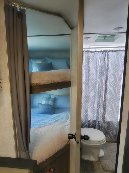 RV rental interior featuring a compact bathroom with shower curtain and toilet, plus a cozy bedroom with bed and privacy curtain.. Gulf Stream Kingsport 2022