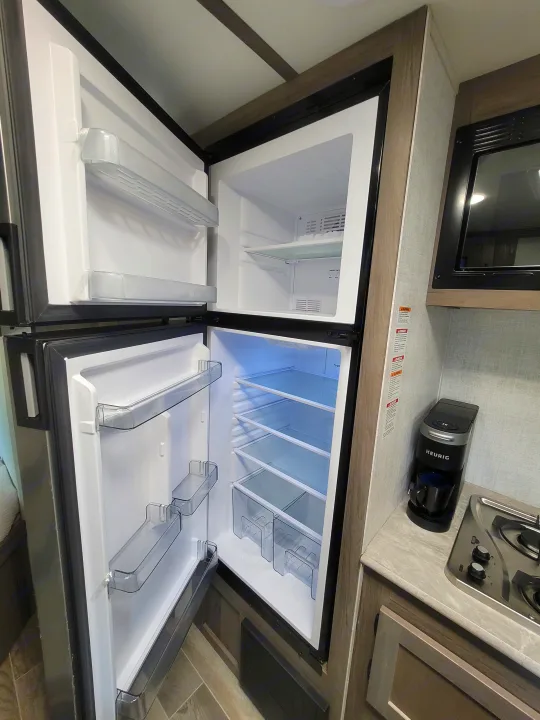 RV rental kitchen featuring an open refrigerator with visible shelves and door bins, plus microwave, stove, and Keurig.. Gulf Stream Kingsport 2022