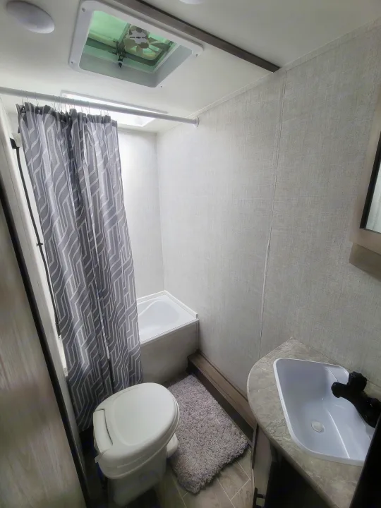 Angled view of an RV rental's bathroom: white sink, toilet, tub, and a gray geometric shower curtain create a compact space.. Gulf Stream Kingsport 2022