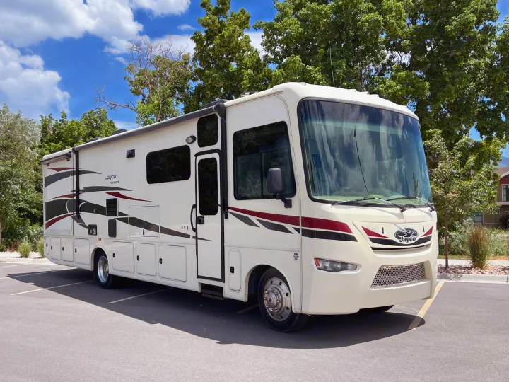 White Jayco Precept RV rental with red/black graphics, parked on asphalt under a blue sky, ready for travel & outdoor adventures.. Jayco Precept 2016
