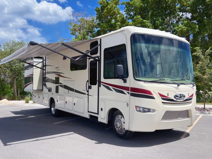 Cream Jayco Precept Class A RV rental with extended awning & slide-out, parked on asphalt under blue sky.. Jayco Precept 2016
