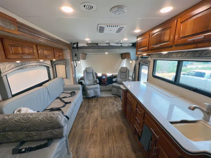 Spacious RV rental interior features light wood flooring, a gray sofa, kitchen counter, and cockpit area.. Jayco Precept 2016
