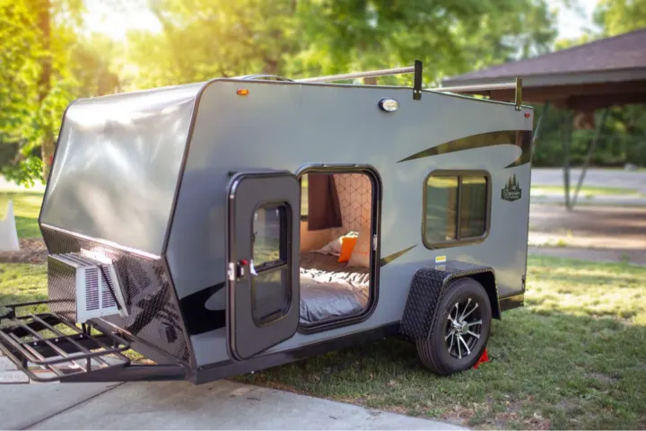 Explore this compact gray RV rental's open door to a cozy bed, perfect for your next outdoor camping adventure.. Superior Lite Camper Deluxe 2022