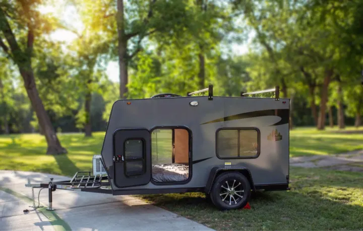 A modern, dark grey teardrop-style RV rental sits on a concrete pad at a sunny campsite, door open to reveal a bed.. Superior Lite Camper Deluxe 2022