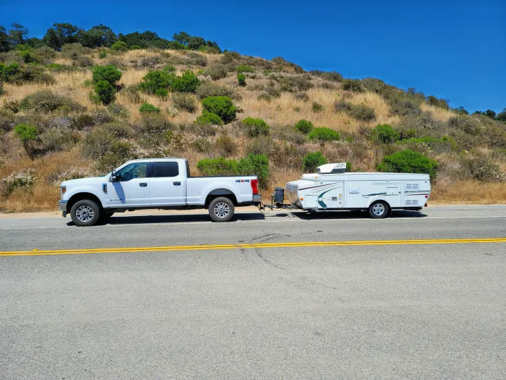 White Ford F-Series pickup towing a Starcraft pop-up camper on a dry hillside road. Great for an RV rental trip!. Starcraft Centennial 2005
