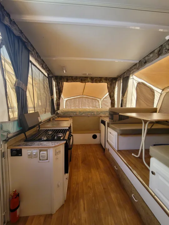Interior of a compact RV rental, featuring a kitchen, dinette, and tent-style pop-out beds. Ready for adventure!. Starcraft Centennial 2005