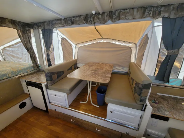 Spacious RV rental pop-up camper interior with dinette, bed, and compact kitchen for comfortable travel.. Starcraft Centennial 2005