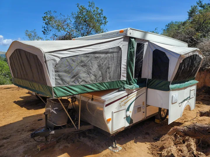 Bright pop-up camper RV rental, white & green, set up on sandy ground outdoors. StarCraft brand visible, ready for adventure.. Starcraft Centennial 2005