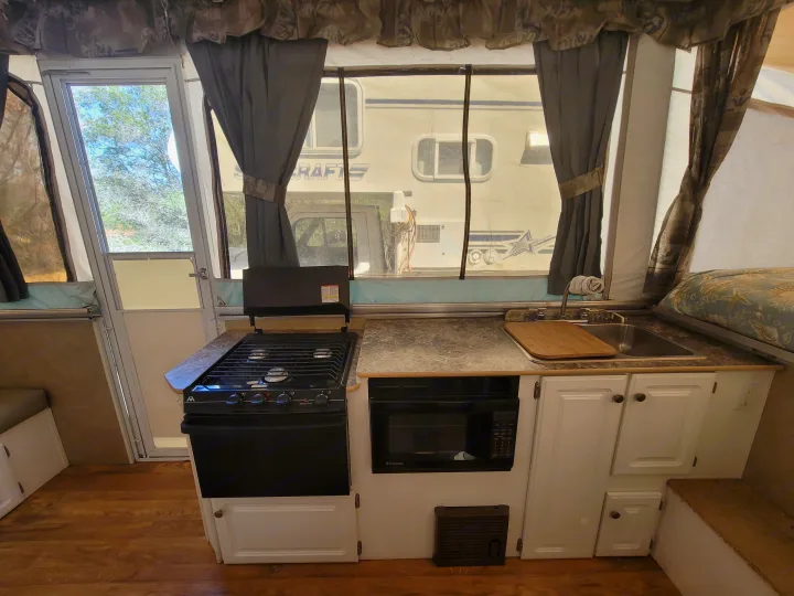 Compact RV rental interior featuring a kitchen with stove, microwave, sink, and a cozy bed area, perfect for travel.. Starcraft Centennial 2005