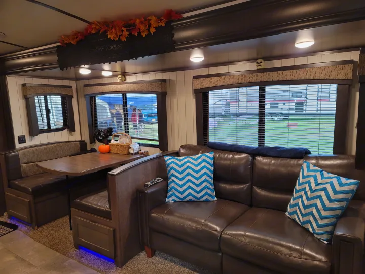 RV rental interior: cozy living space with a brown sofa, dining booth, and festive autumn decorations.. Crossroads RV Sunset Trail Super Lite 2018