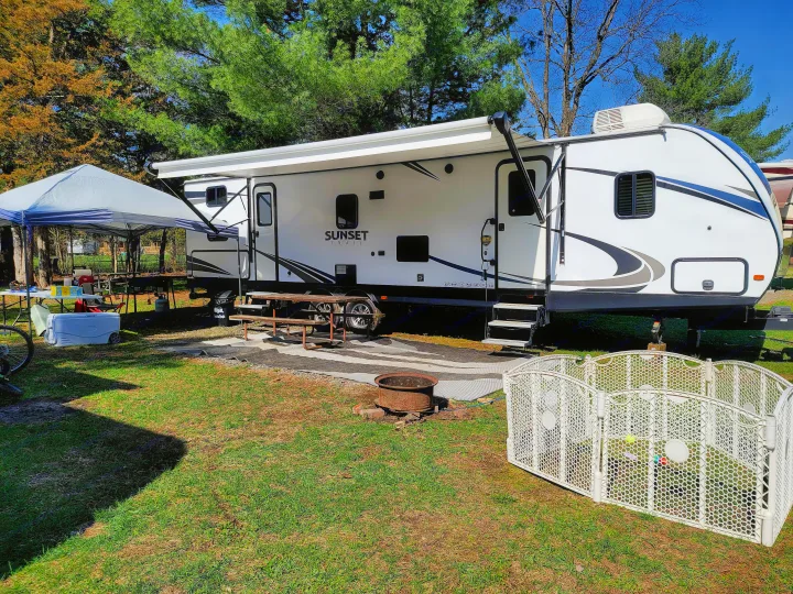 RV rental campsite setup featuring a white travel trailer, large canopy, picnic table, fire pit, and playpen.. Crossroads RV Sunset Trail Super Lite 2018