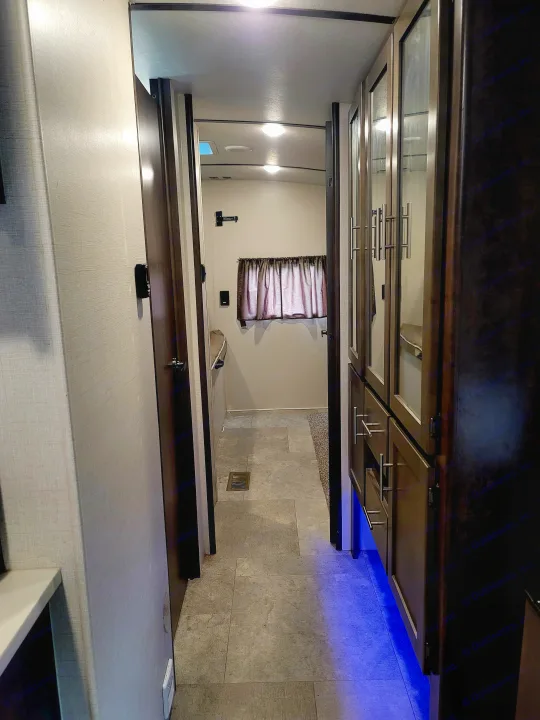 Cozy RV rental interior: A well-lit hallway leads past dark wood cabinets with blue lighting into a spacious bedroom area.. Crossroads RV Sunset Trail Super Lite 2018