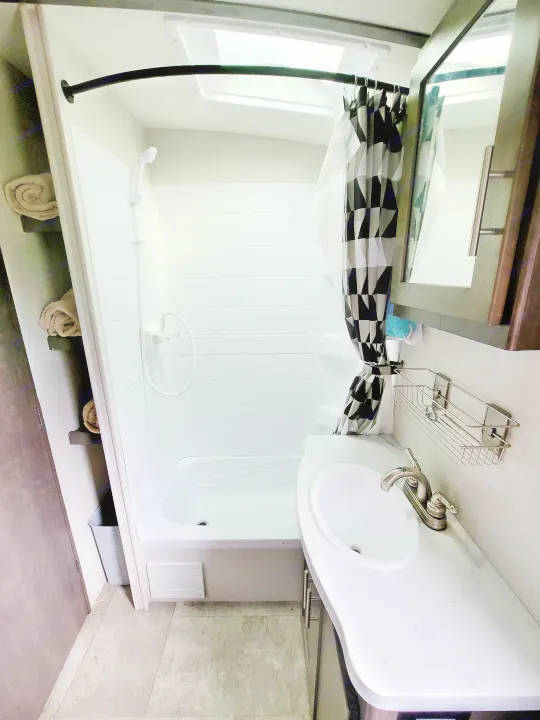 An RV rental bathroom, showcasing a shower/tub combo, vanity sink, and shelving with fresh towels.. Crossroads RV Sunset Trail Super Lite 2018