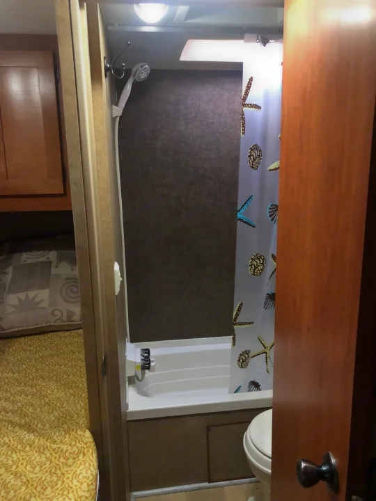 RV rental bathroom features a beach-themed shower curtain (starfish, seashells), handheld shower, and toilet. Clean, compact space.. Forest River Cherokee 2015