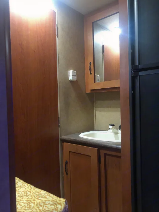 RV rental interior: compact bathroom with sink, mirrored cabinet, thermostat, & wood accents. Perfect for road trips.. Forest River Cherokee 2015