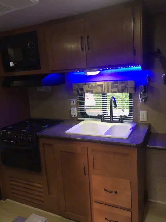 RV rental kitchen interior: compact design with wooden cabinets, sink, and cool blue LED lighting.. Forest River Cherokee 2015