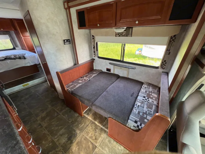Inside an RV rental: a versatile living area featuring a convertible dinette bed and a peek into the cozy bedroom.. Winnebago Chalet 2013
