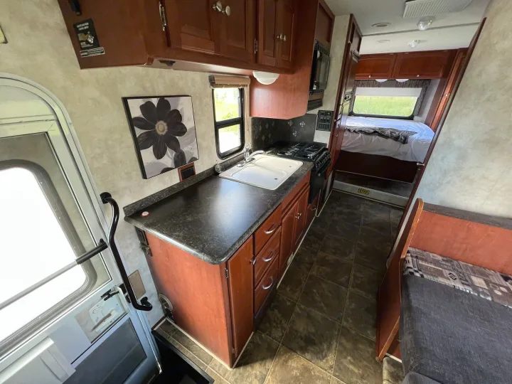Inside this RV rental: a compact kitchen with sink/stove, a comfortable bedroom, and seating, ready for adventure.. Winnebago Chalet 2013