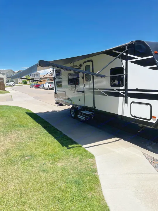 White & black RV rental with an extended awning, parked on a sunny driveway. Your next adventure awaits!. Grand Design Imagine XLS 2021