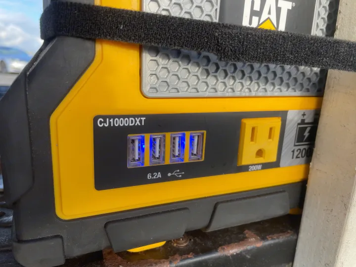 A yellow CAT CJ1000DXT portable power station with 4 glowing USB ports and AC outlet, useful for RV rental power & jump-starting.. Ford Transit Connect 2010