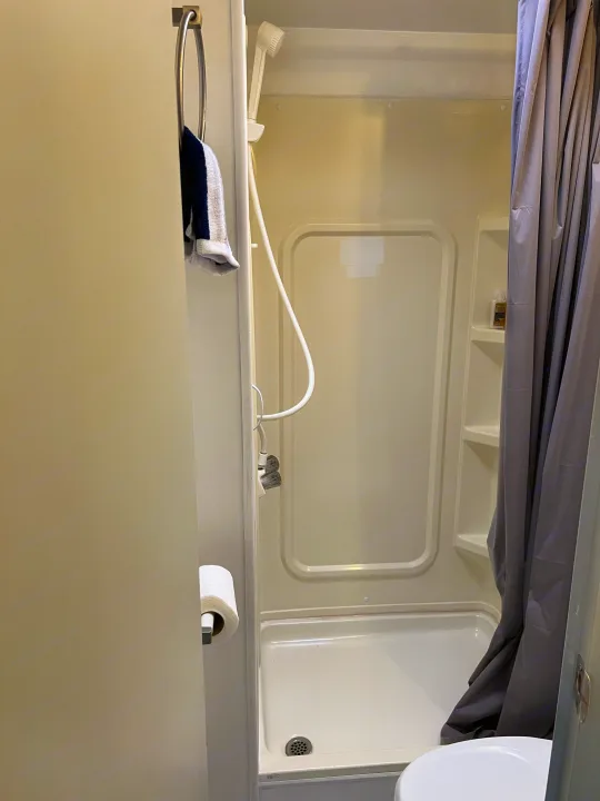 Inside a compact RV rental bathroom, featuring a shower with handheld head, toilet, and towel ring.. Dutchmen Sport 2004