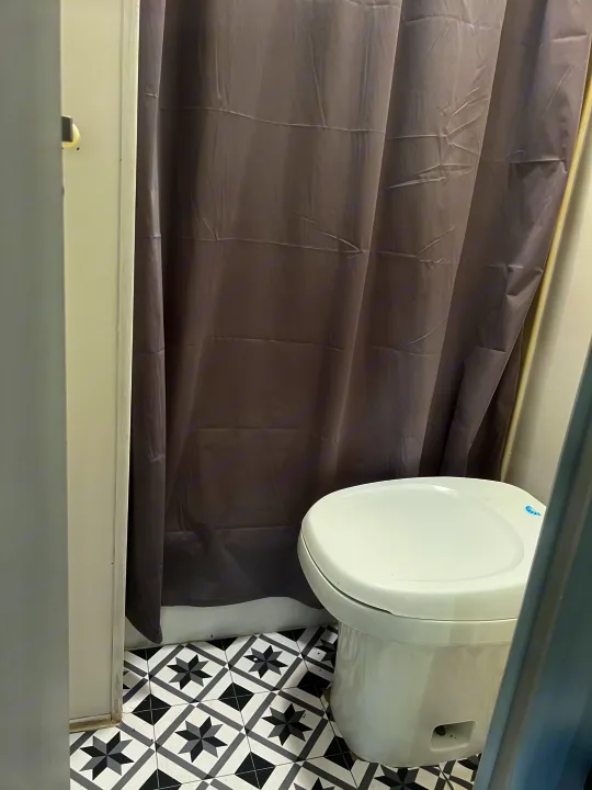 RV rental bathroom features a white toilet, gray shower curtain, and a striking black and white patterned tile floor.. Dutchmen Sport 2004