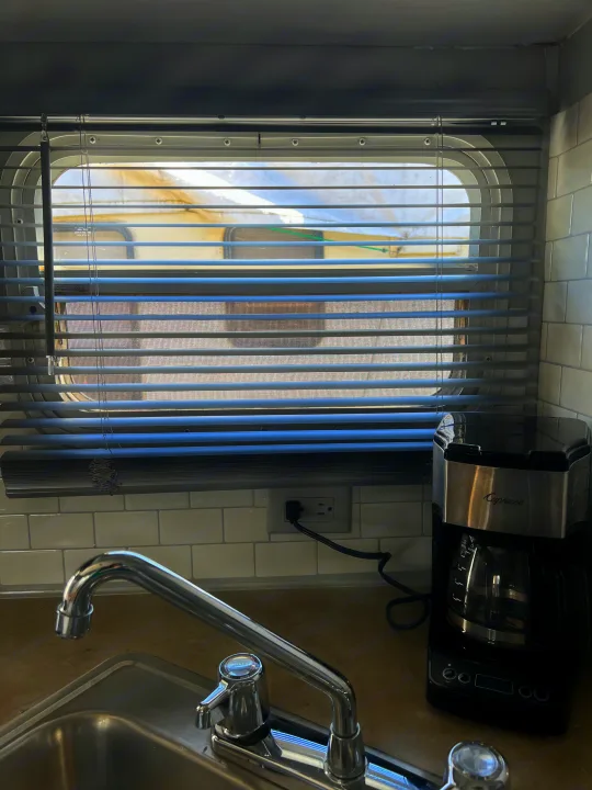 Inside an RV rental: Compact kitchen featuring a sink, Capresso coffee maker, and a window with gray blinds.. Dutchmen Sport 2004