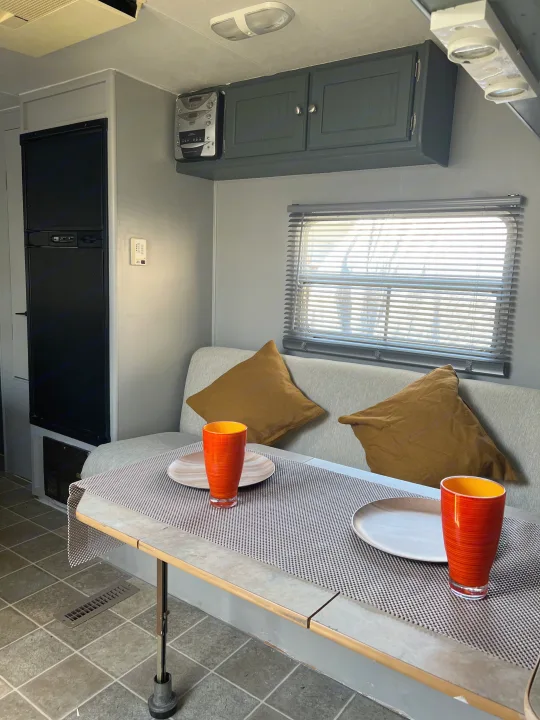 Cozy rv rental interior: dining nook with table, bench seating, plates, glasses.. Dutchmen Sport 2004