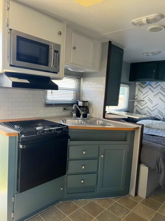 Bright, updated RV rental interior featuring a kitchen with stove, sink, microwave, and dark teal cabinets.. Dutchmen Sport 2004