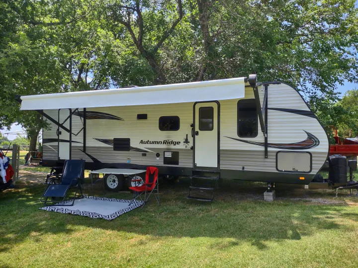Enjoy this Autumn Ridge travel trailer RV rental, set up with an awning, outdoor chairs, and a rug on the grass for a relaxing camp.. Starcraft Autumn Ridge Outfitter 2019