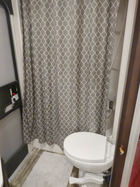 Compact RV rental bathroom features a white toilet & patterned gray shower curtain, offering privacy in a tight space.. Starcraft Autumn Ridge Outfitter 2019