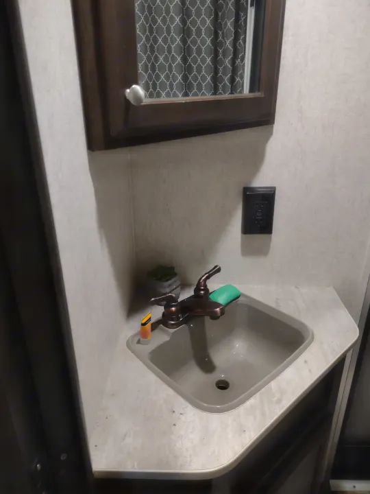 Compact RV rental kitchen with sink, faucet, USB outlet, and patterned window blind, offering essential amenities.. Starcraft Autumn Ridge Outfitter 2019