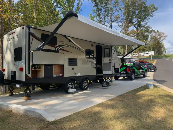 An RV rental, a Passport travel trailer, set up at campsite 120 with an extended awning. A branded truck is parked nearby.. Keystone RV Passport Elite 2017