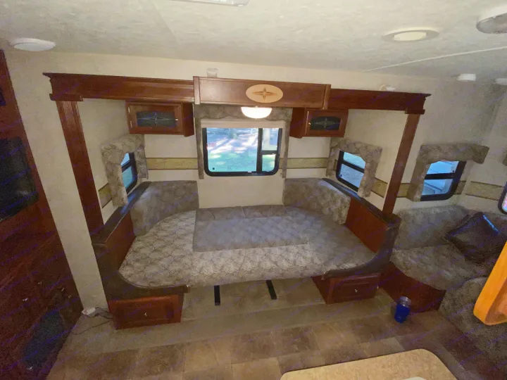 This inviting RV rental interior features a spacious U-shaped dinette converting to a bed, dark wood cabinetry, and windows.. Forest River Rockwood Windjammer 2012
