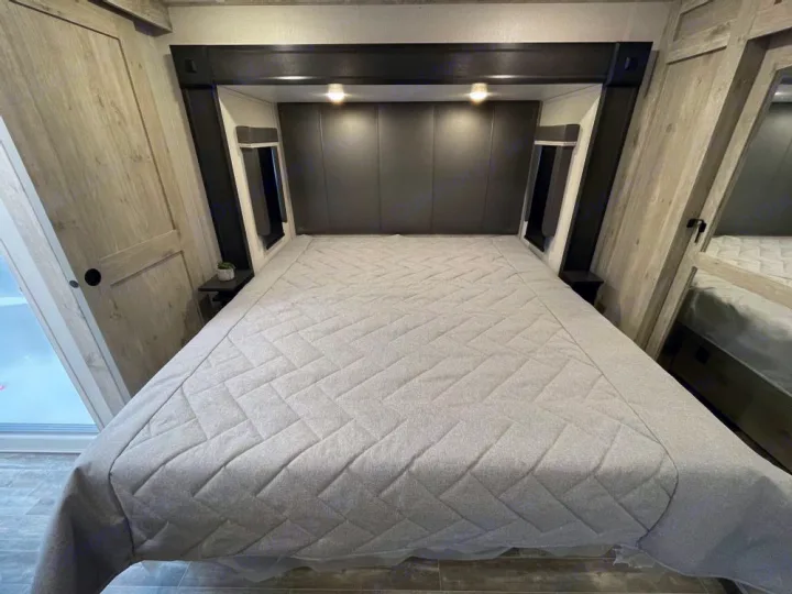 Inside an RV rental bedroom: a comfortable bed with a modern headboard, integrated nightstands, and light wood storage.. Keystone RV Alpine Avalanche Edition 2025