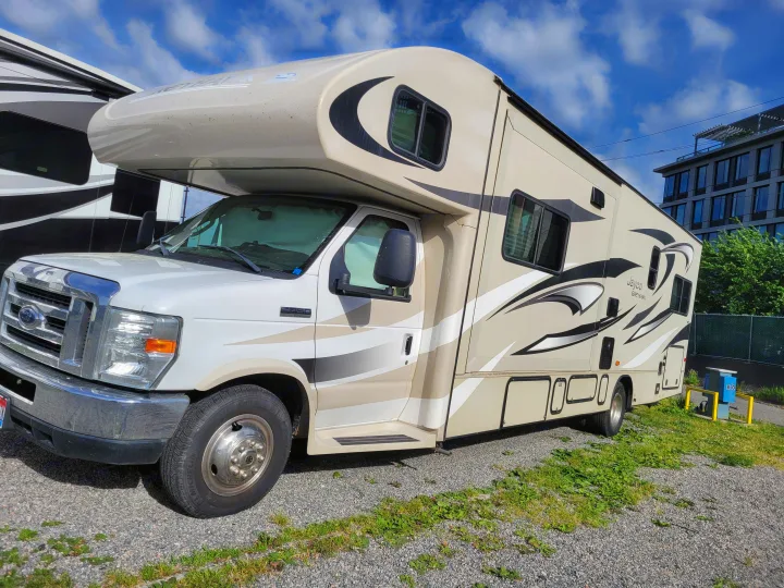 Jayco Greyhawk RV rental: This beige motorhome with black/white graphics is parked on gravel, ready for your next adventure.. Jayco Greyhawk 2014