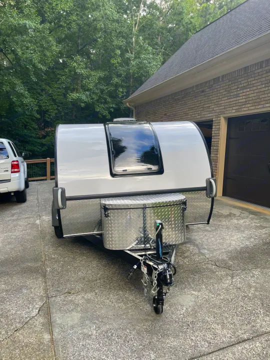 Compact white travel trailer, ideal for an rv rental adventure, parked in a driveway. Features a large front window & storage box.. nuCamp RV T@G XL 6 wide 2022