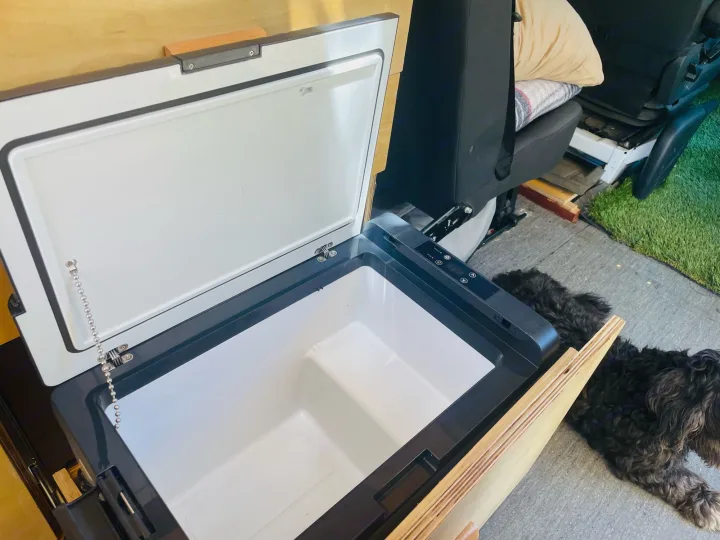 Essentials for your RV rental: An open portable fridge, ready for food & drinks. A fluffy dog lounges on the floor.. Dodge Sprinter Van 2007