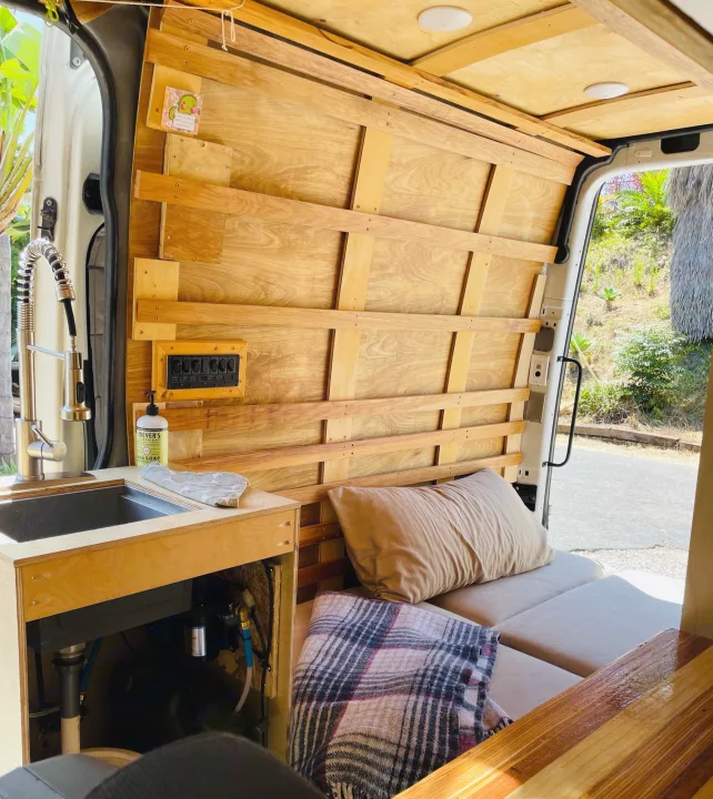 Cozy custom RV rental interior with wooden walls, sink, control panel, and bed area. Perfect for mobile living.. Dodge Sprinter Van 2007