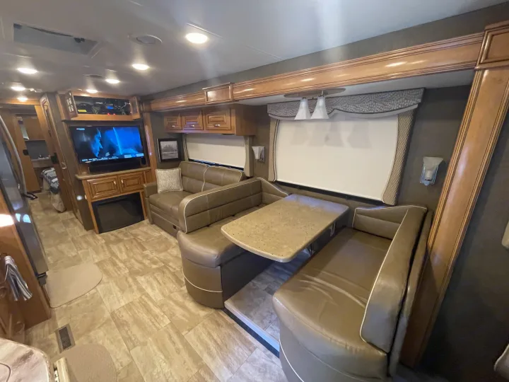 Comfortable RV rental living area featuring a dining booth, sofa, TV, and built-in cabinetry.. Thor Challenger 2017